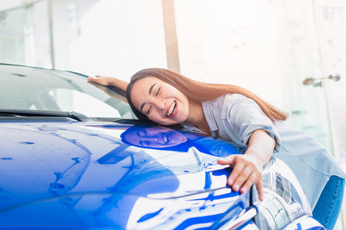 Teen girl happily hugging a new blue car, illustrating parents gifting 17YO golden child an expensive car.