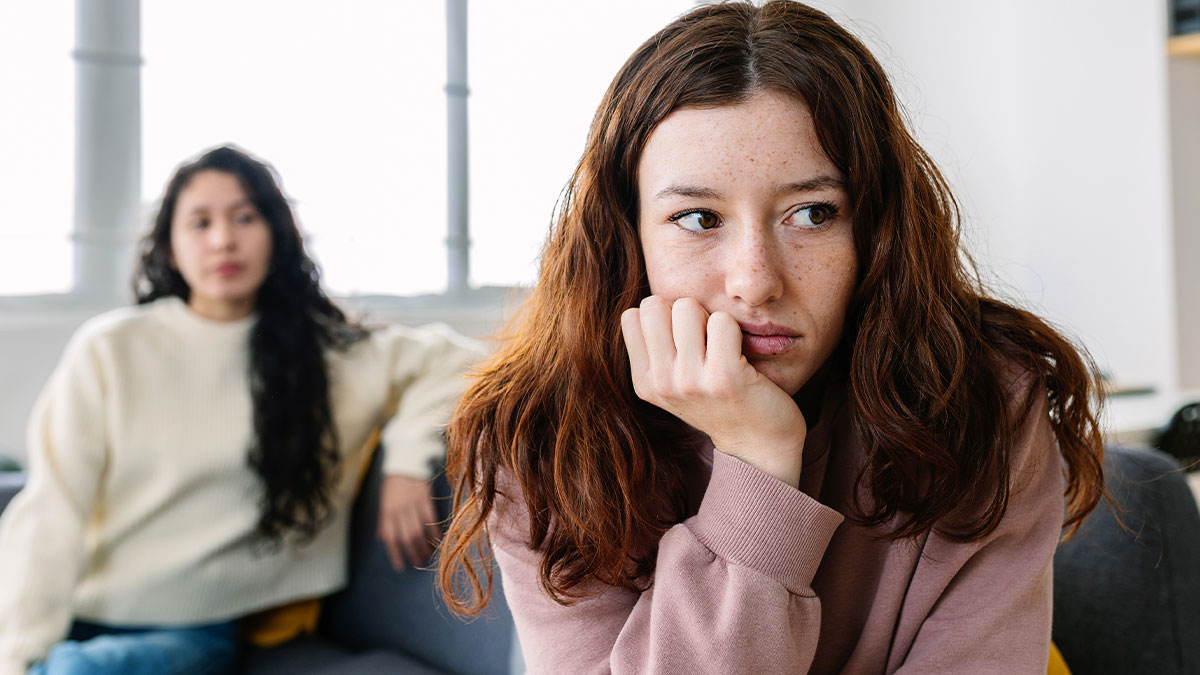 Woman feeling upset and betrayed as petty sister ruins her life instead of choosing therapy, both sitting on a couch indoors.