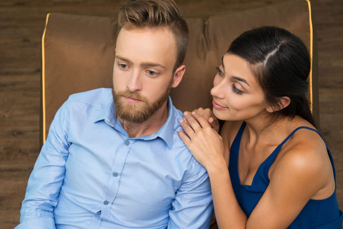 Young couple with the man looking worried while the woman gently touches his shoulder, depicting relationship conflict and regret.