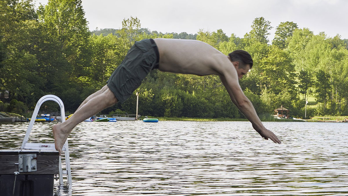 Man in green shorts diving off dock into lake surrounded by trees, illustrating simple car stuff skills concept.