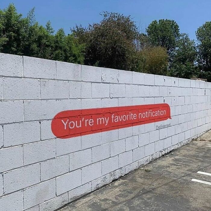 Graffiti on a white brick wall showing a red text bubble with the message you're my favorite notification, girly memes theme.