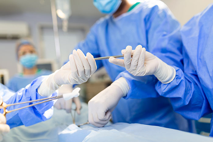 Surgeons in blue scrubs performing a surgical procedure in a hospital operating room with medical instruments.