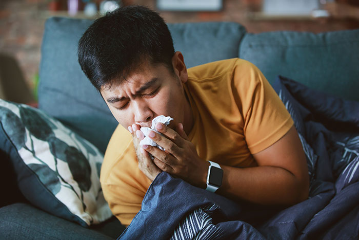 Man sneezing into tissue at home, illustrating unexpected health issues leading to hospital visits and surgery instead.