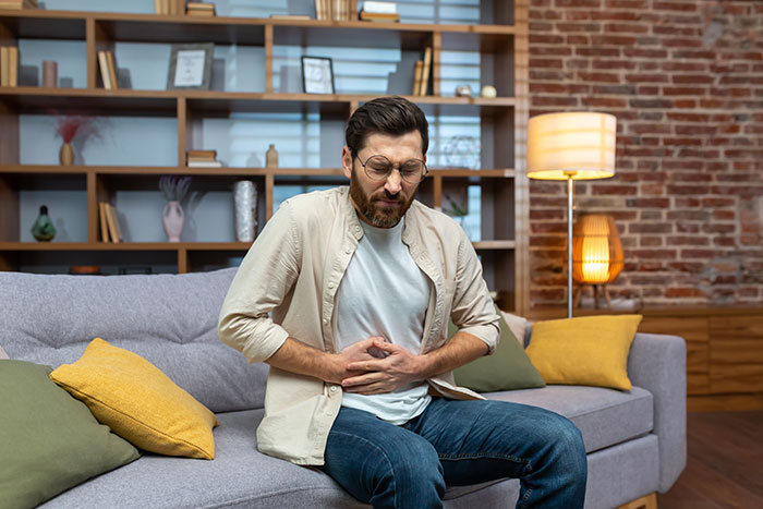 Man sitting on couch holding stomach in pain, illustrating times people came to hospital for surgery instead of a minor issue.