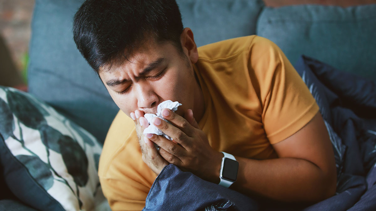 Man holding tissue to nose, looking ill on couch, illustrating people needing surgery after hospital visits for small issues.