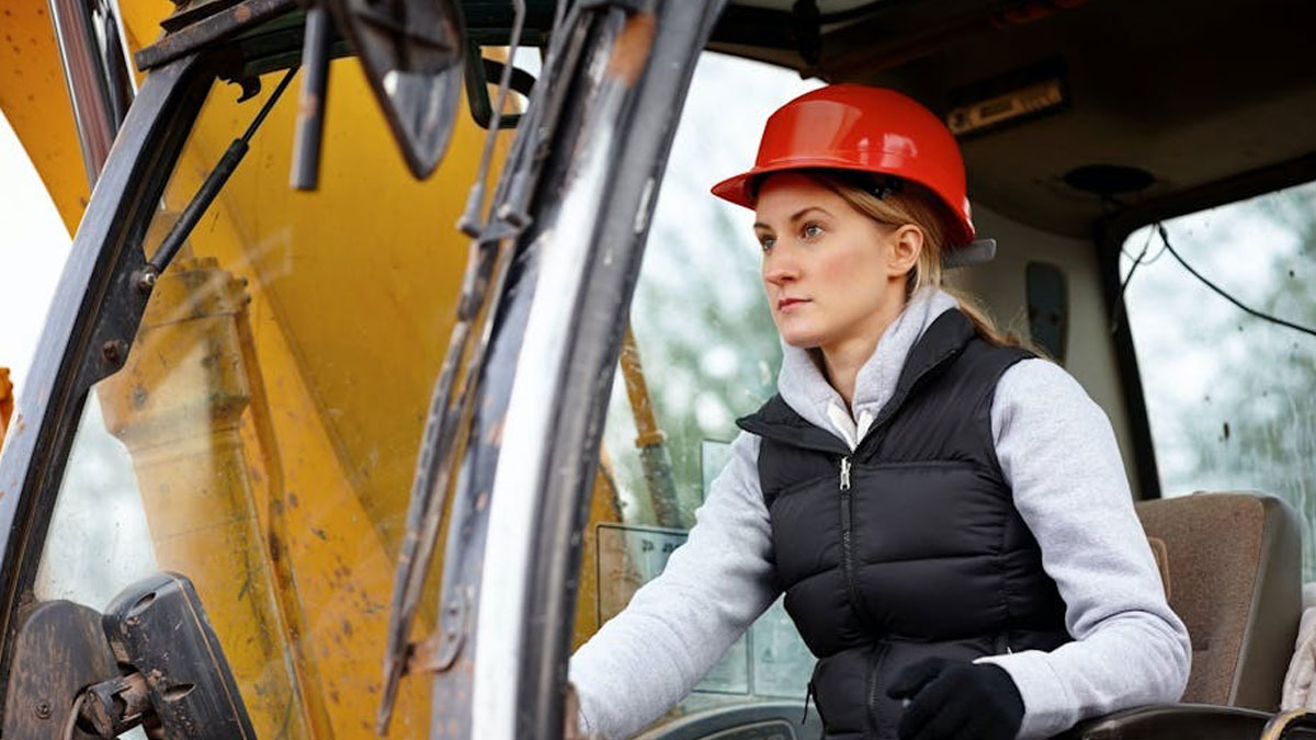 Woman in a red hard hat operating heavy machinery, illustrating themes of dystopic society and unsettling work conditions.