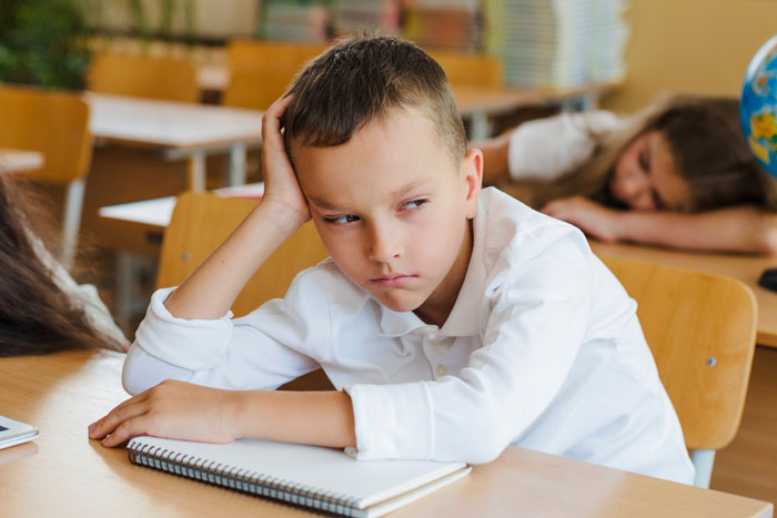 Young boy in classroom looking upset, representing challenges faced by diabetic kid banned from checking glucose at school.