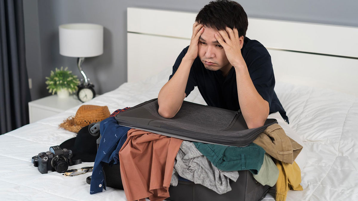 Young adult man upset on bed with packed suitcase and clothes, illustrating a 20YO mooching off parents story.