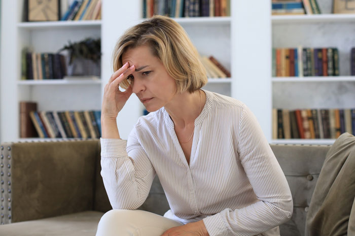 Woman sitting on couch looking stressed and worried, representing parents dealing with a 20-year-old mooching off them. Woman sitting on couch looking stressed and worried, representing parents dealing with a 20-year-old mooching off them.
