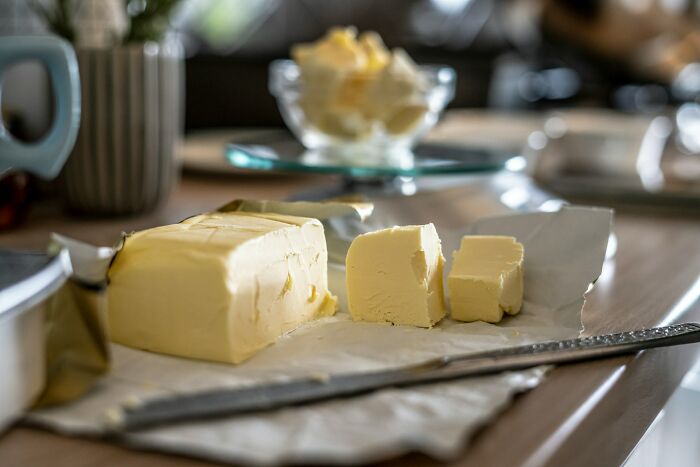 Block of butter partially sliced on parchment paper with a knife on a kitchen counter, unrelated to shrimp jello.