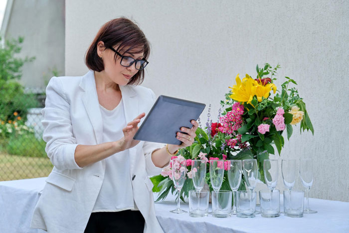 Woman in white blazer using tablet near wedding table with flowers and glassware, capturing Star Wars wedding preparations. Woman in white blazer using tablet near wedding table with flowers and glassware, capturing Star Wars wedding preparations.