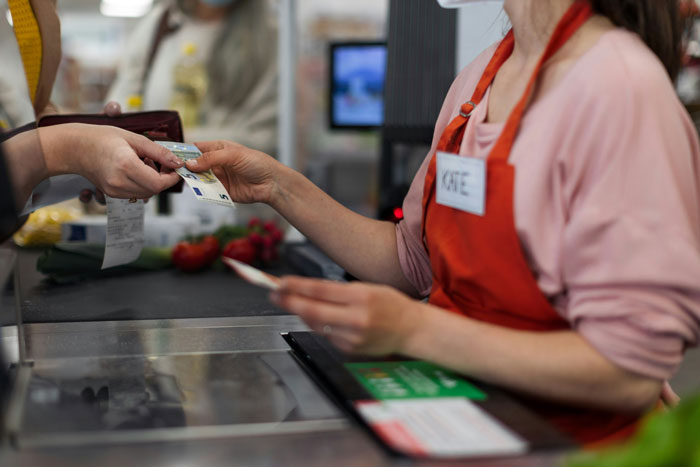Customer handing money to cashier at convenience store counter during purchase transaction.