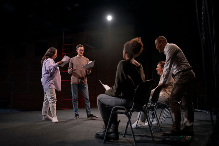 Group of actors rehearsing on stage under spotlight, focused on steering career against dreams in performing arts. Group of actors rehearsing on stage under spotlight, focused on steering career against dreams in performing arts.