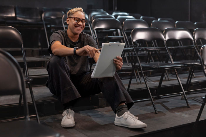 Person reviewing notes on a tablet, smiling while seated among empty chairs, focusing on steering career against dreams. Person reviewing notes on a tablet, smiling while seated among empty chairs, focusing on steering career against dreams.