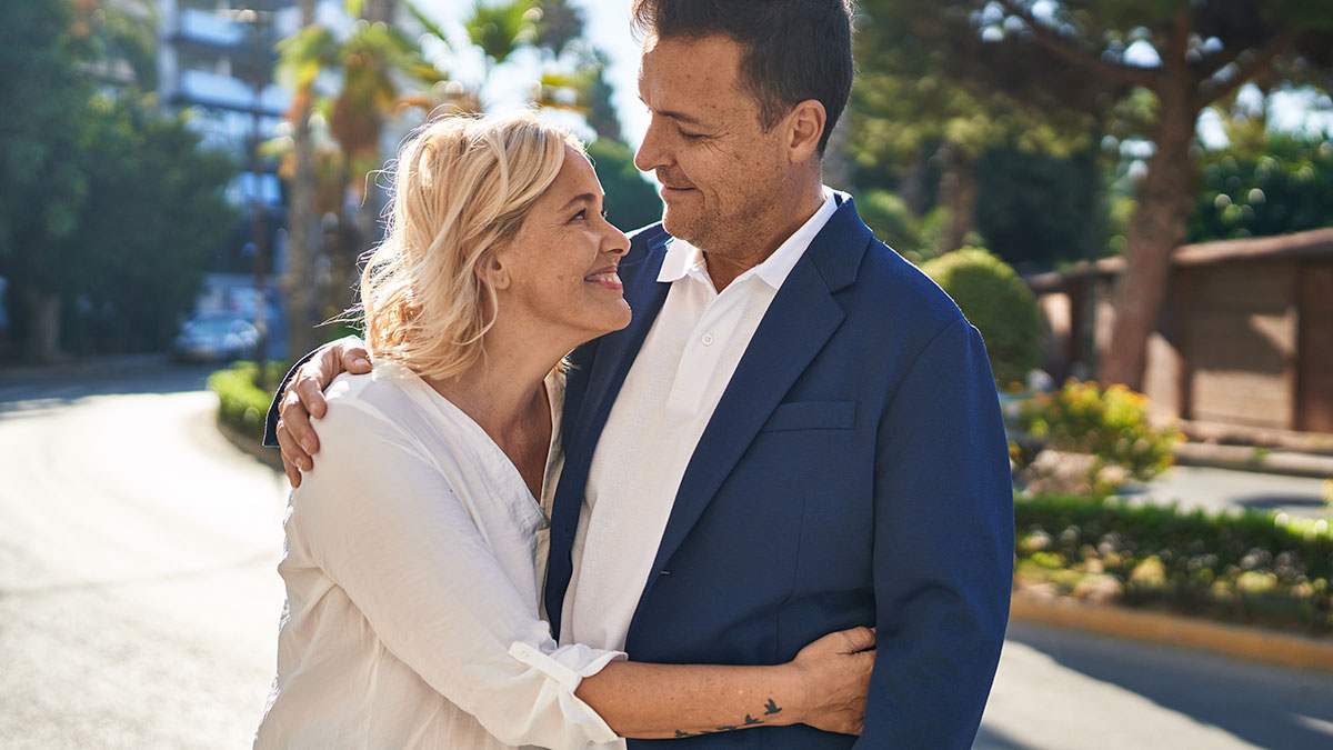 Middle-aged stepdad and wife embracing outdoors, expressing pride and complex emotions about family blending.