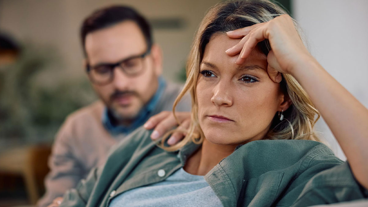 Worried woman sits with supportive partner in background, reflecting tension from family issues with stepmom and kids.