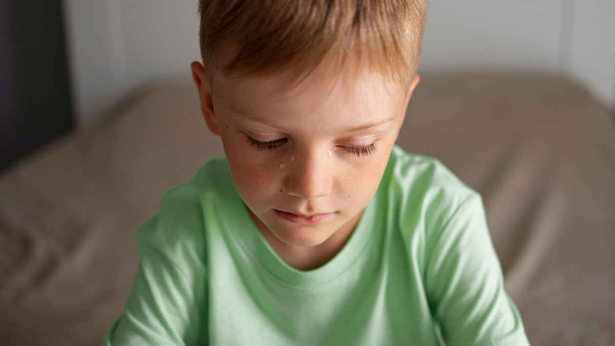 Young boy with tears on his face sitting on a bed, related to mom sparks debate about biological daughteru2019s biggest room