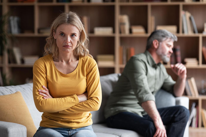 Stepmom and husband sitting apart looking upset in living room, family tension over stepdaughter's heirloom jewelry dispute. Stepmom and husband sitting apart looking upset in living room, family tension over stepdaughter's heirloom jewelry dispute.