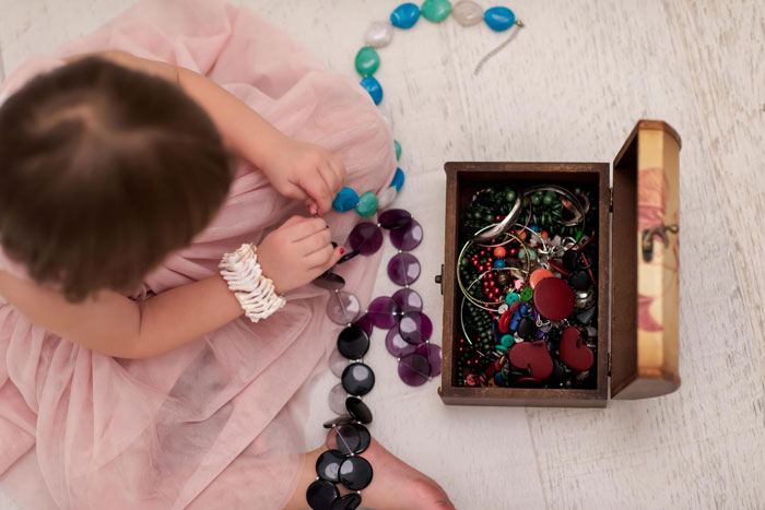 Young child in pink dress playing with broken heirloom jewelry next to an open wooden box filled with colorful accessories. Young child in pink dress playing with broken heirloom jewelry next to an open wooden box filled with colorful accessories.