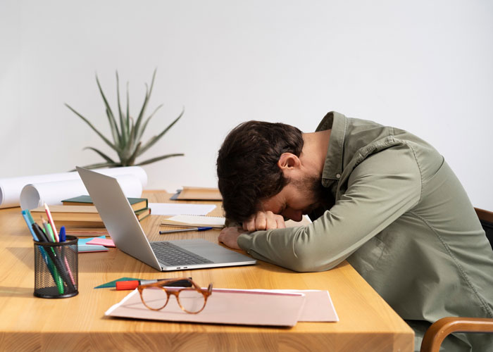 Man at desk with head down feeling burnout in a hostile work environment with toxic bosses and workplace stress. Man at desk with head down feeling burnout in a hostile work environment with toxic bosses and workplace stress.