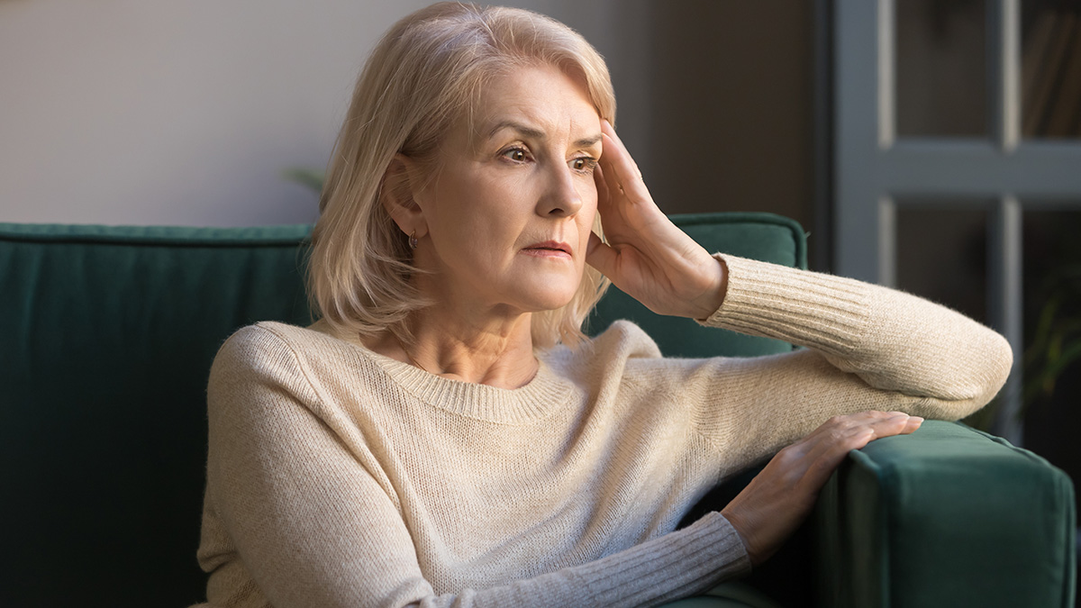 Elderly woman sitting on couch looking worried and deep in thought about strange 911 operator calls she received.