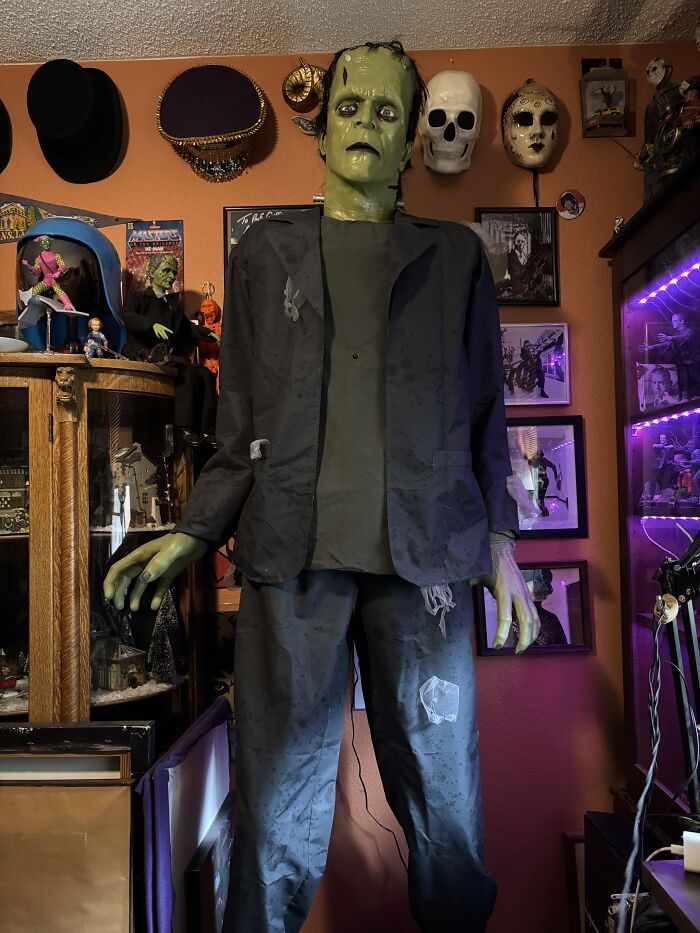 A life-sized Frankenstein figure in a cluttered room filled with spooky masks and eerie decorations inside a stranger’s home.