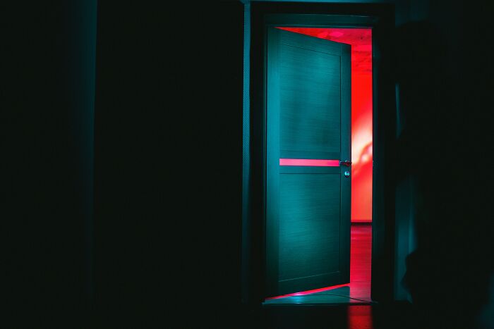 Dimly lit open door with eerie red light inside, evoking the strange and unsettling sights workers encounter in homes.