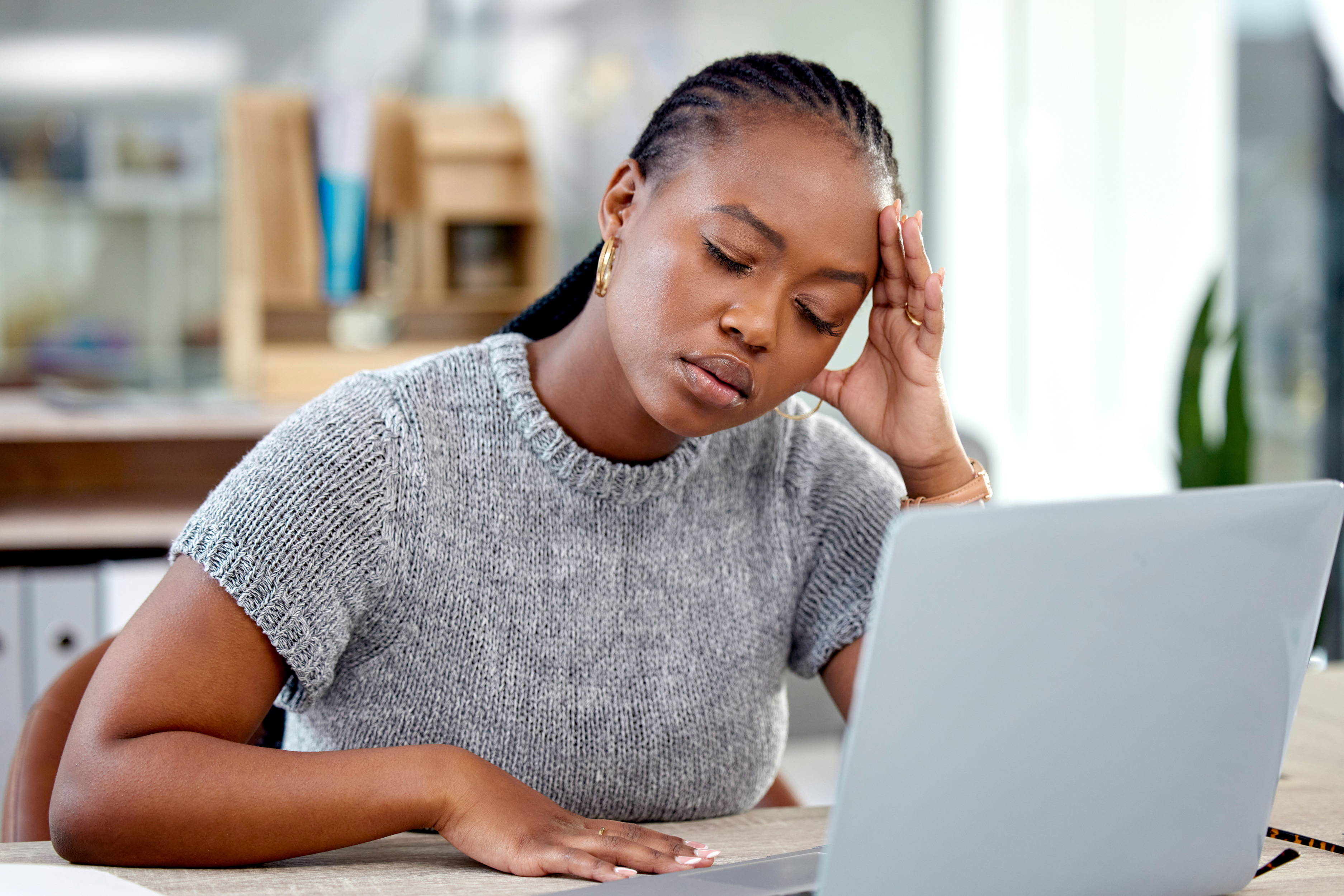 African American woman looking stressed while working on a laptop, highlighting issues of job offers and name bias. African American woman looking stressed while working on a laptop, highlighting issues of job offers and name bias.
