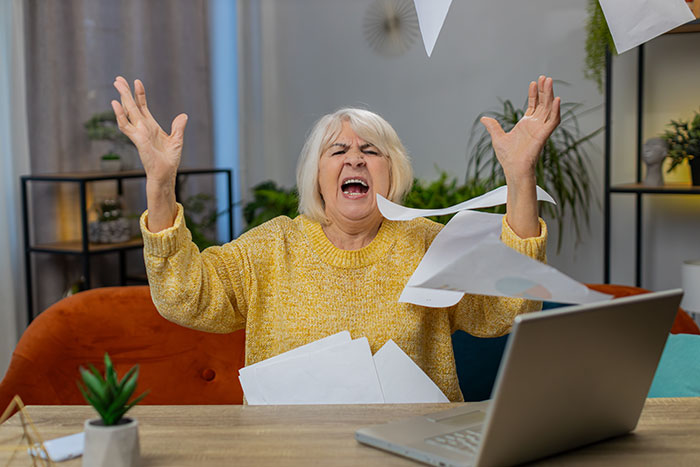 Angry older woman throwing papers while sitting at a desk with a laptop, illustrating mother accuses daughter kidnapping. Angry older woman throwing papers while sitting at a desk with a laptop, illustrating mother accuses daughter kidnapping.