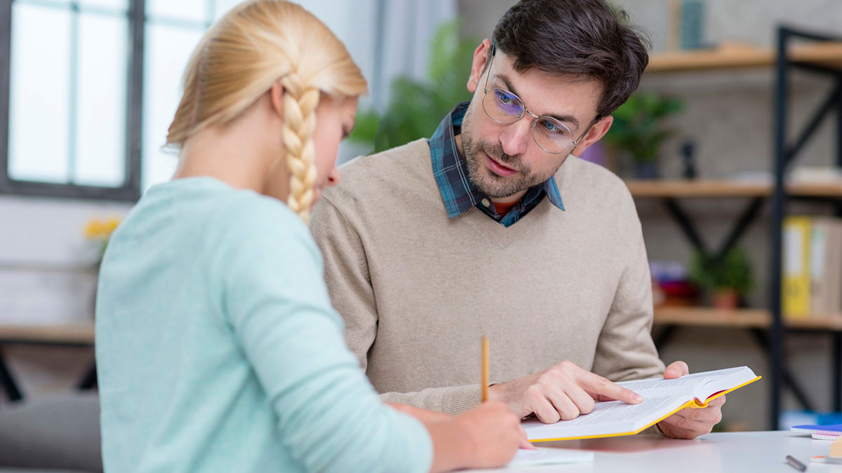 Man and young woman discussing text, former student interaction captured in an indoor study setting.
