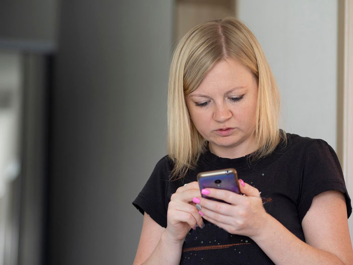 Woman with blonde hair wearing black shirt, looking at smartphone, texting and sharing screenshots about former student situation. Woman with blonde hair wearing black shirt, looking at smartphone, texting and sharing screenshots about former student situation.