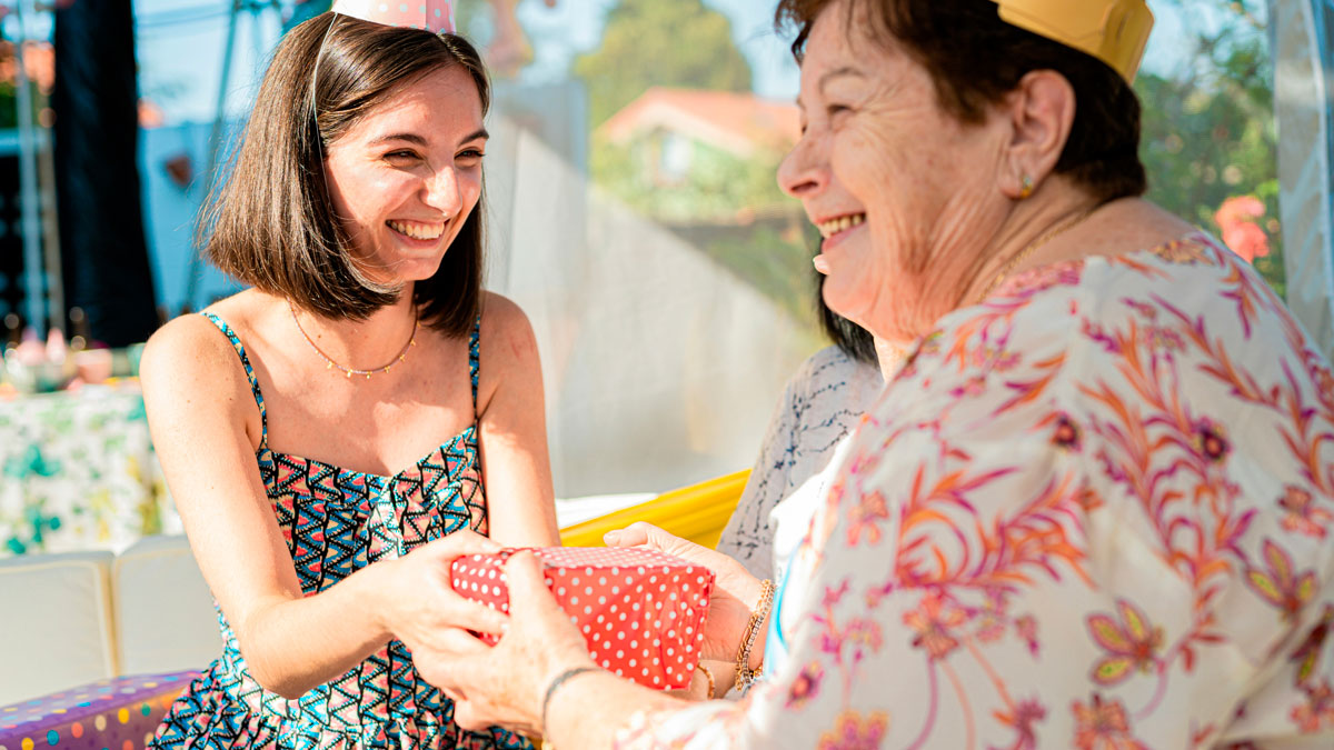 Teen girl smiling and receiving a birthday gift from an elderly woman at a family celebration outdoors.