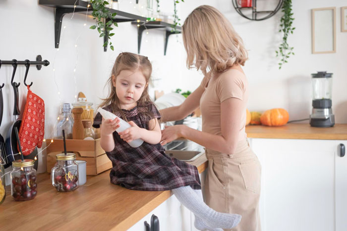 Woman prioritizes her bio kid over stepdaughters while their mom reacts angrily in a sunlit kitchen setting.