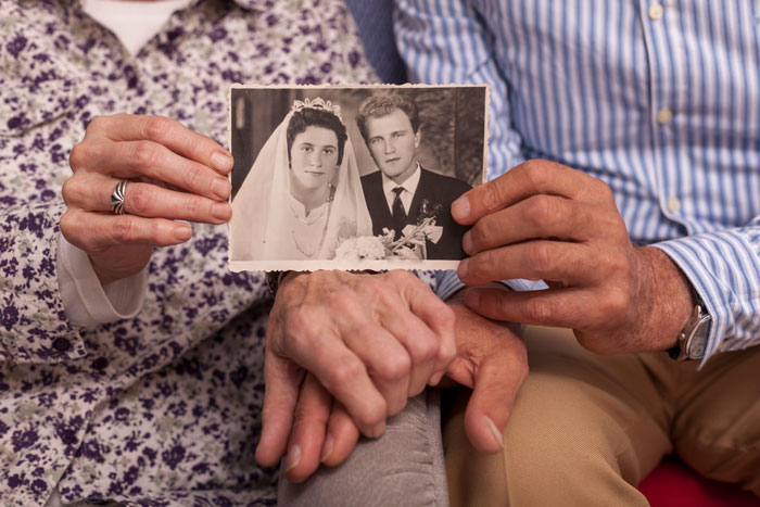 Elderly couple holding a vintage wedding photo representing heirlooms and family legacy in a blended family context.