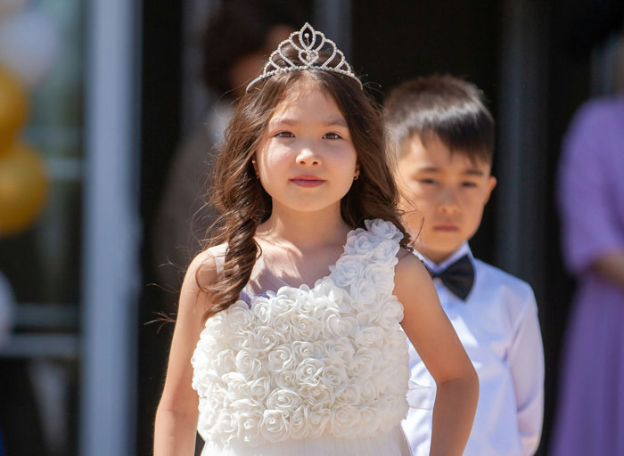 Young girl wearing a floral dress and tiara with a boy in formalwear behind her, highlighting stepdaughters and bio kid conflict.