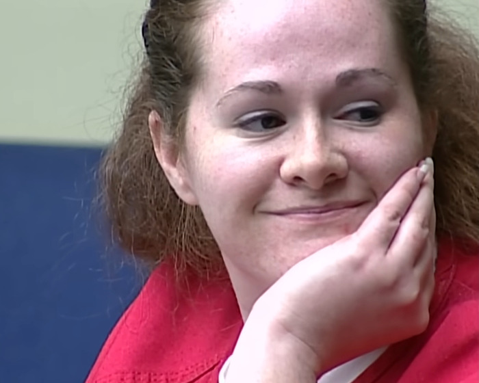 Woman in a red shirt sitting and smiling slightly, related to capital punishment for stabbing and pentagram carving case. Woman in a red shirt sitting and smiling slightly, related to capital punishment for stabbing and pentagram carving case.