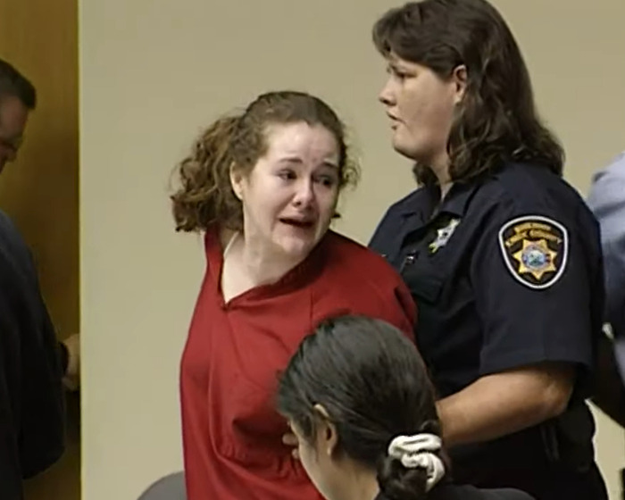 Woman in red prison uniform being escorted by officer during court hearing for capital punishment case. Woman in red prison uniform being escorted by officer during court hearing for capital punishment case.
