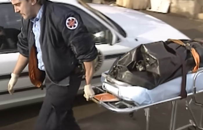 Man in uniform pushing stretcher with covered body bag near white vehicle in an outdoor setting related to punishment case. Man in uniform pushing stretcher with covered body bag near white vehicle in an outdoor setting related to punishment case.