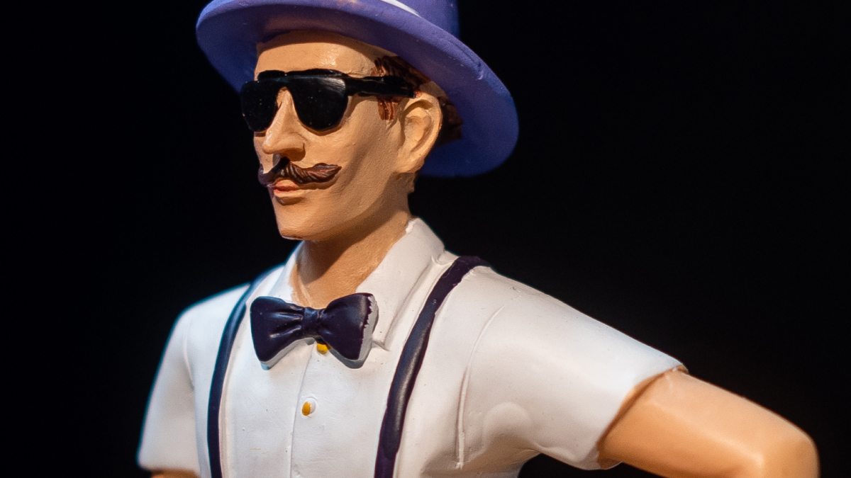 Figurine of a man wearing sunglasses, a hat, bow tie, and suspenders representing performative male culture concept.