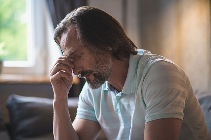 Middle-aged man in a striped polo shirt looking stressed and contemplative, representing husband unattracted to plastic surgery wife. Middle-aged man in a striped polo shirt looking stressed and contemplative, representing husband unattracted to plastic surgery wife.