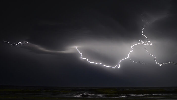 Lightning striking over a dark ocean under powerful weather conditions showcasing incredible planetary weather records.