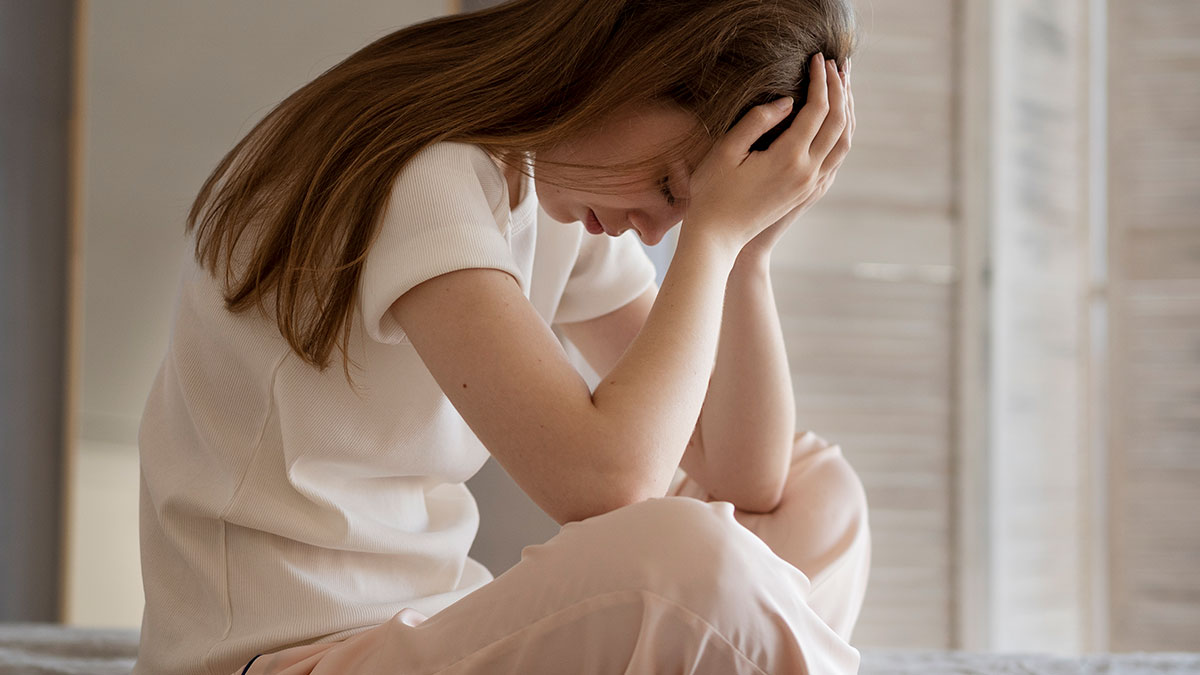 Tired mom sitting with head in hands, feeling let down and overwhelmed in a quiet, softly lit room.