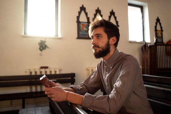 Religious man holding a book in a church, reflecting on faith, causing tension with coworkers at work. Religious man holding a book in a church, reflecting on faith, causing tension with coworkers at work.