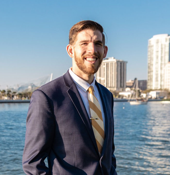Smiling man in a suit near waterfront with city buildings in the background representing Florida man incident.