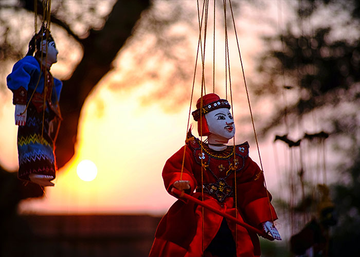 Traditional puppets dressed in colorful attire hanging by strings at sunset, representing unique college courses.
