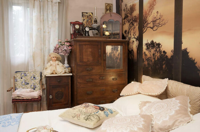 Vintage bedroom with 50 dolls, wooden furniture, and floral decor in a chaotic fairytale Airbnb setting. Vintage bedroom with 50 dolls, wooden furniture, and floral decor in a chaotic fairytale Airbnb setting.