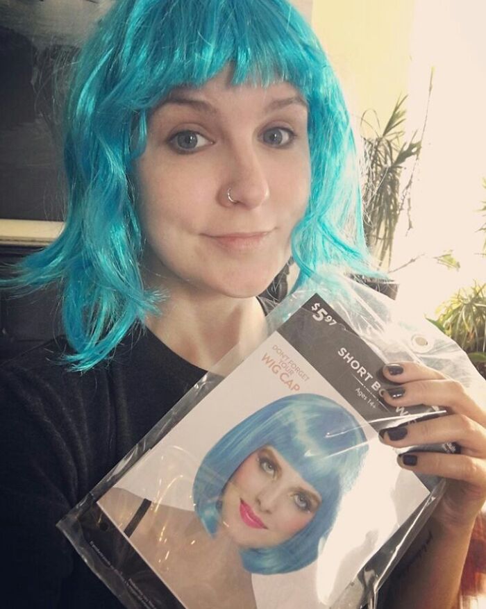 Person wearing a blue wig holding the packaged wig showing a funny Halloween fail with costume expectations versus reality.