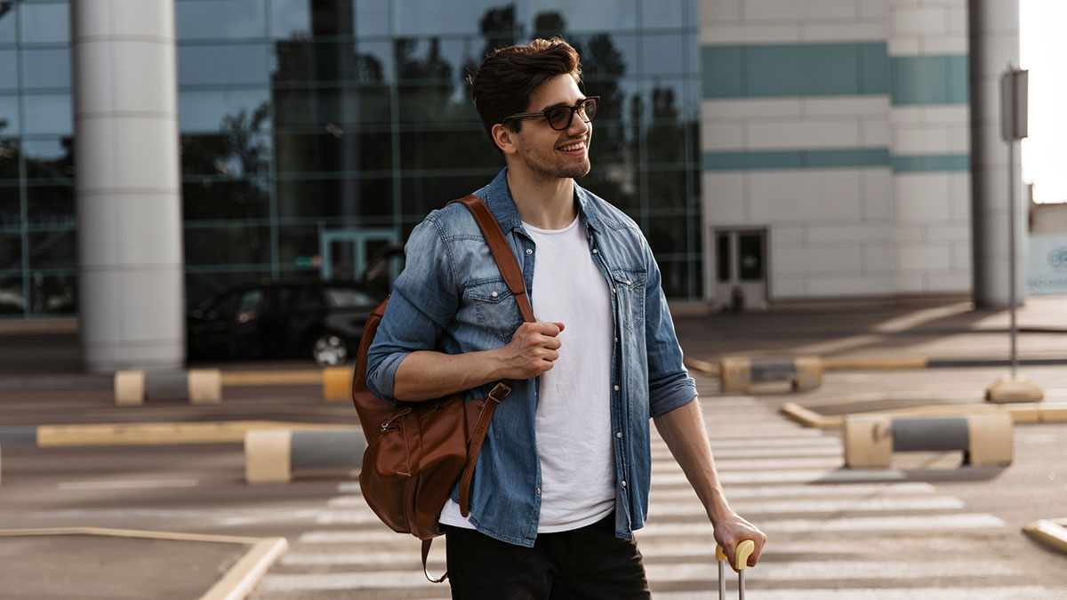 Young man with sunglasses and backpack smiling outside, symbolizing a surprise family visit organized during surgery planning.