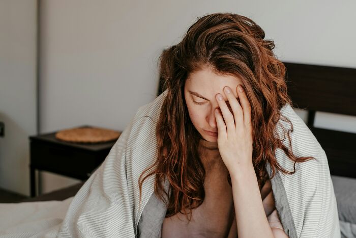 Young woman with long red hair sitting in bed wrapped in a blanket looking stressed, reflecting worst first opinions doctors hear.