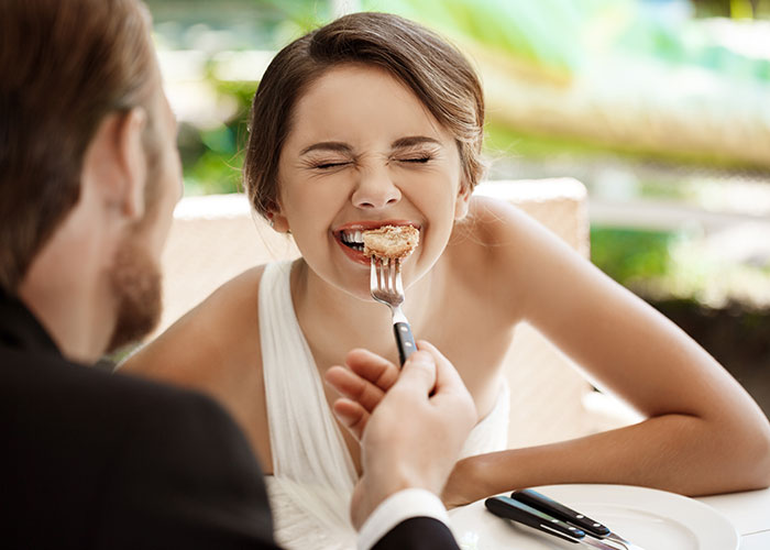 Bride smiling with eyes closed being fed a small piece of dessert by groom, highlighting wedding vendors and allergy issues. Bride smiling with eyes closed being fed a small piece of dessert by groom, highlighting wedding vendors and allergy issues.